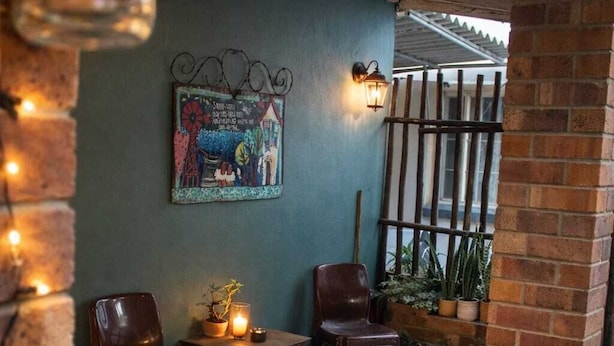 A cozy patio area with two wooden chairs, a small table, a wall-mounted light, and a potted plant. - Amazing 2-bedroom cottage in Graafwater, perfect for a relaxing getaway (Graafwater)