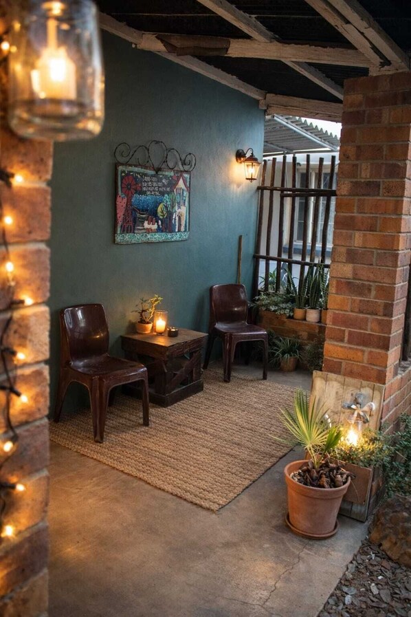 A cozy patio area with two wooden chairs, a small table, a wall-mounted light, and a potted plant.