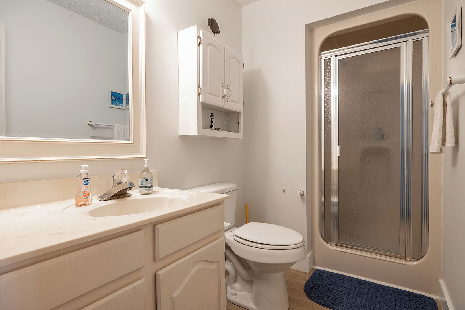 A bathroom with a white sink, toilet, and shower. There are two bottles of hand soap on the sink.