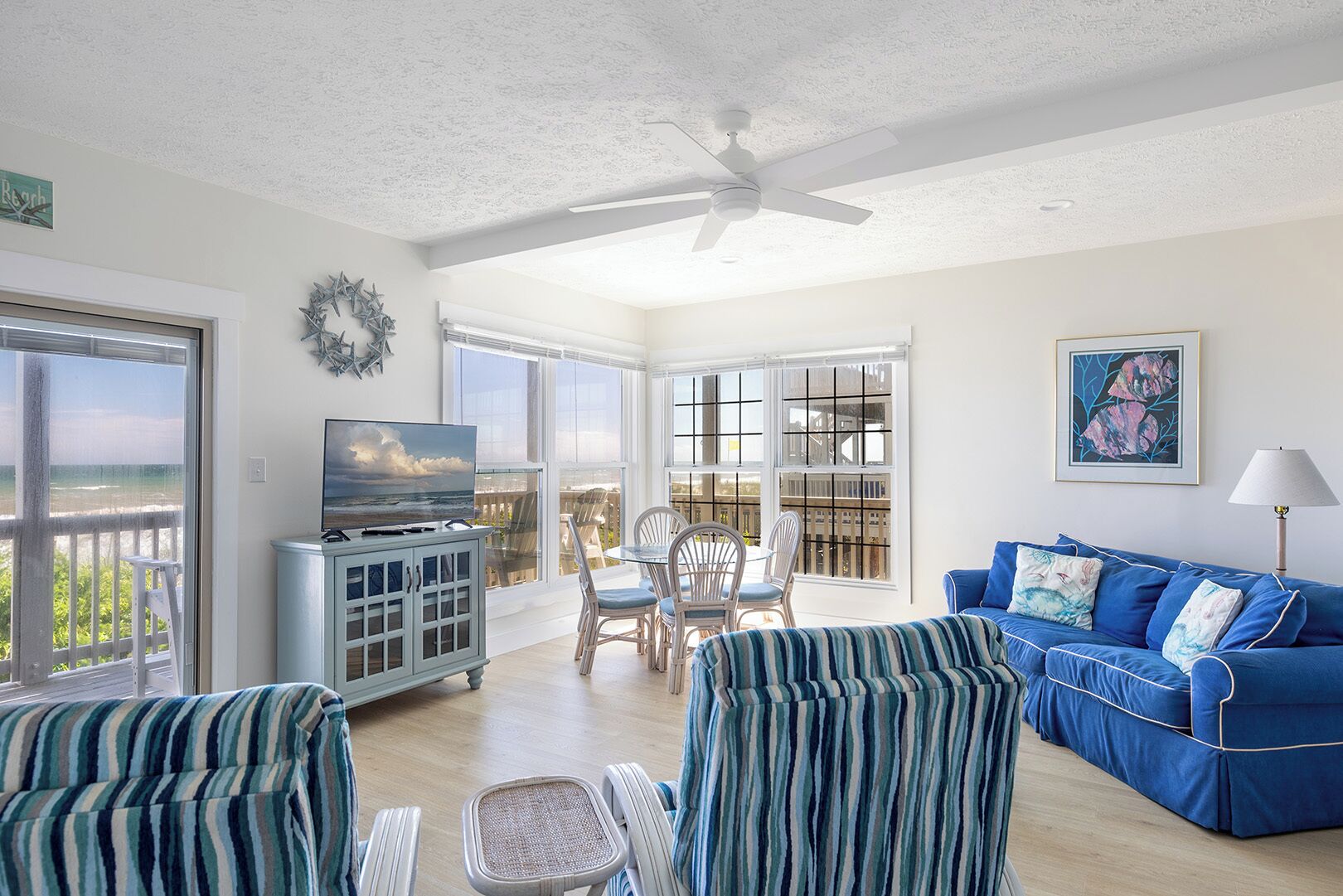 A spacious living room with a large TV, a blue sofa, and a dining area with chairs.