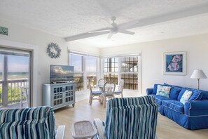 Ein geräumiges Wohnzimmer mit großem Fernseher, einem blauen Sofa und einem Essbereich mit Stühlen.