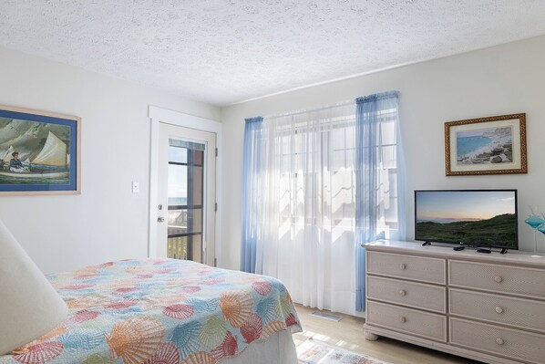 Ein Schlafzimmer mit einem Bett, einem Schminktisch, einem Fernseher und einer Tür, die auf einen Balkon führt.
