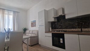A modern kitchen with a gas stove, oven, and white cabinets. There is a dining area with a table and chairs, and a sofa. - Casa di Riccardo Apartment in the living heart of Tuscany between Florence and Pisa (San Miniato)