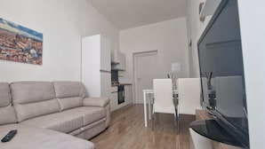 A living room with a sofa, a remote control, a dining area with a table and chairs, a kitchen area, and a TV. - Casa di Riccardo Apartment in the living heart of Tuscany between Florence and Pisa (San Miniato)