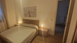 A bedroom with a bed, two bedside tables with lamps, a wall-mounted artwork, and a door leading to another room. - Casa di Riccardo Apartment in the living heart of Tuscany between Florence and Pisa (San Miniato)
