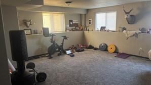 Et hjemmegym med træningsudstyr, et løbebånd, vægte og et gevir monteret på væggen.