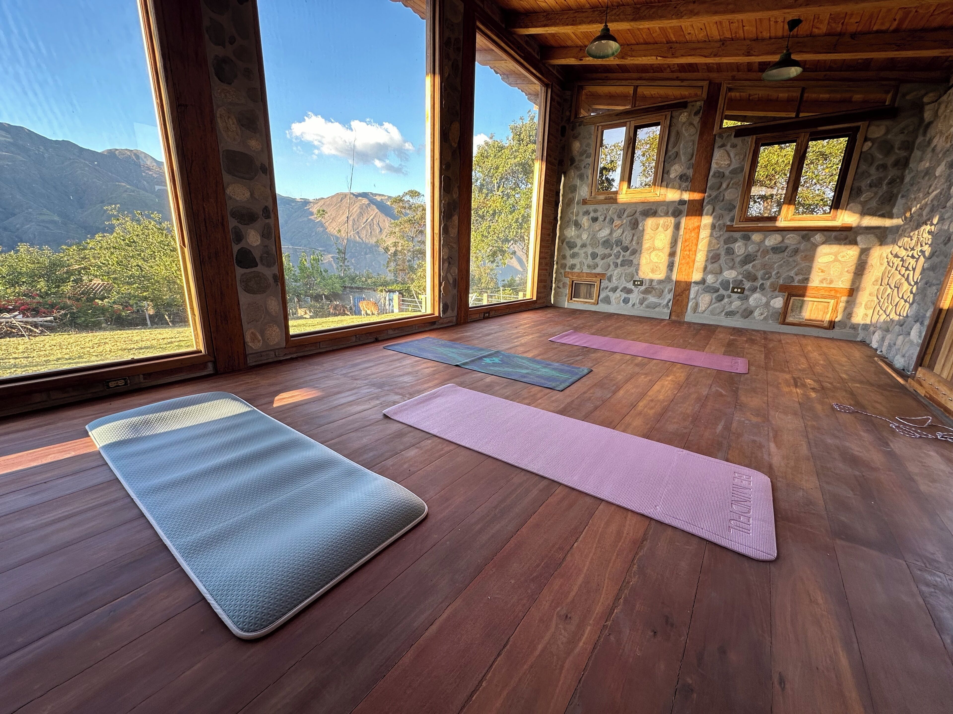 A yoga room with wooden floors, stone walls, and large windows offering mountain views.