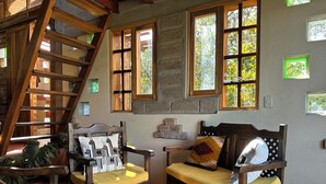 A rustic interior with a wooden staircase, two wooden chairs with cushions, a woven basket, and a brick wall. - La Casita Cabin: Beautiful 1-bedroom cabin in Cahuasquí for a relaxing stay (Calle Bolivar)