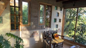 A room with a wooden bed, a wooden chair, a small table, and a large window with a view of greenery. - La Casita Cabin: Beautiful 1-bedroom cabin in Cahuasquí for a relaxing stay (Calle Bolivar)