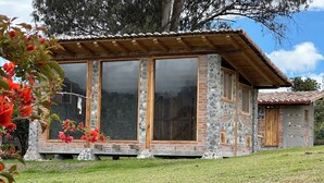 A stone and wood house with large windows and a covered porch. - La Casita Cabin: Beautiful 1-bedroom cabin in Cahuasquí for a relaxing stay (Calle Bolivar)