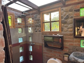 A rustic bathroom with a shower, a toilet, a sink, and a window.