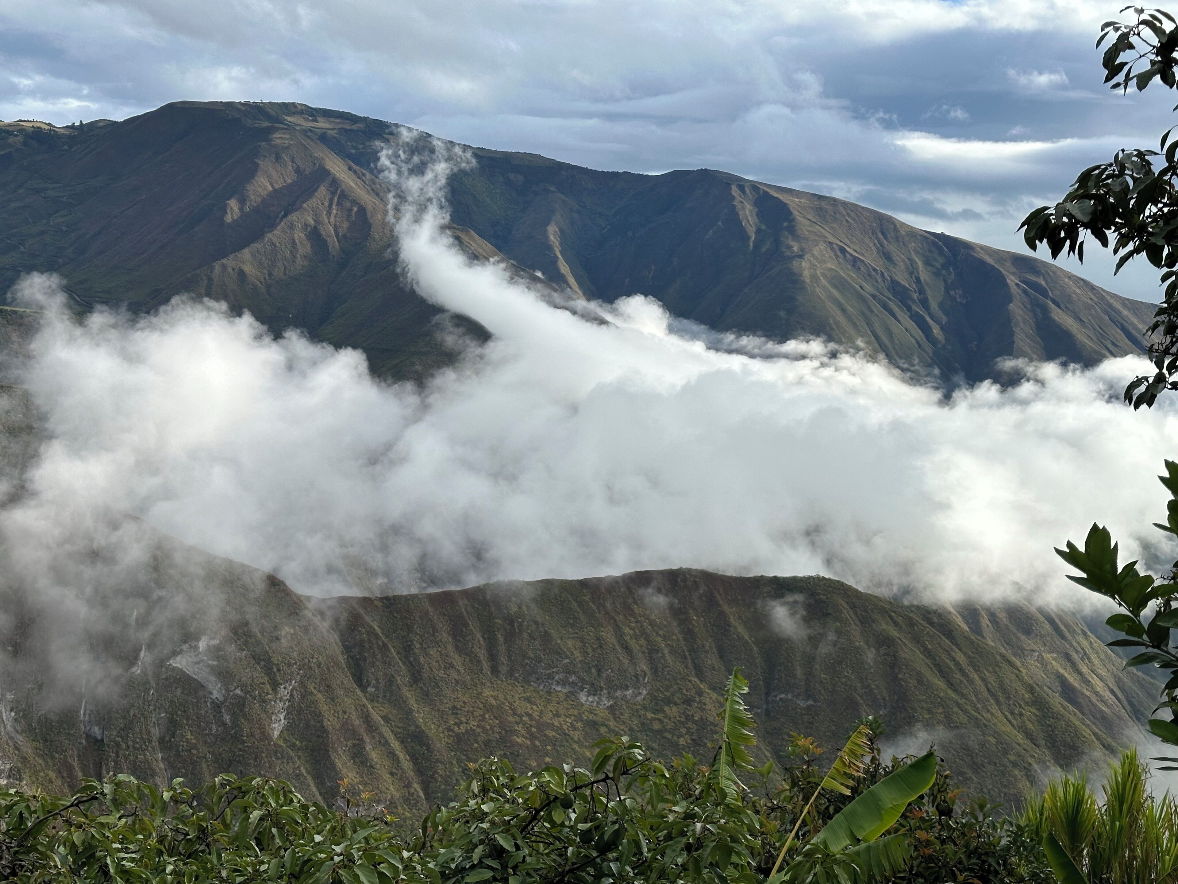 Une montagne dont le sommet est enveloppé de nuages et dont le pied est recouvert d’une végétation luxuriante.