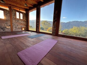 Ett yogarum med trägolv, stora fönster och en vägg av sten.