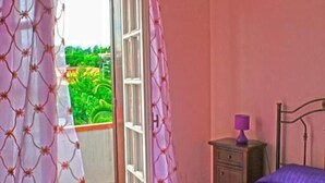 Una habitación con cama, mesita de noche y ventana con cortinas.