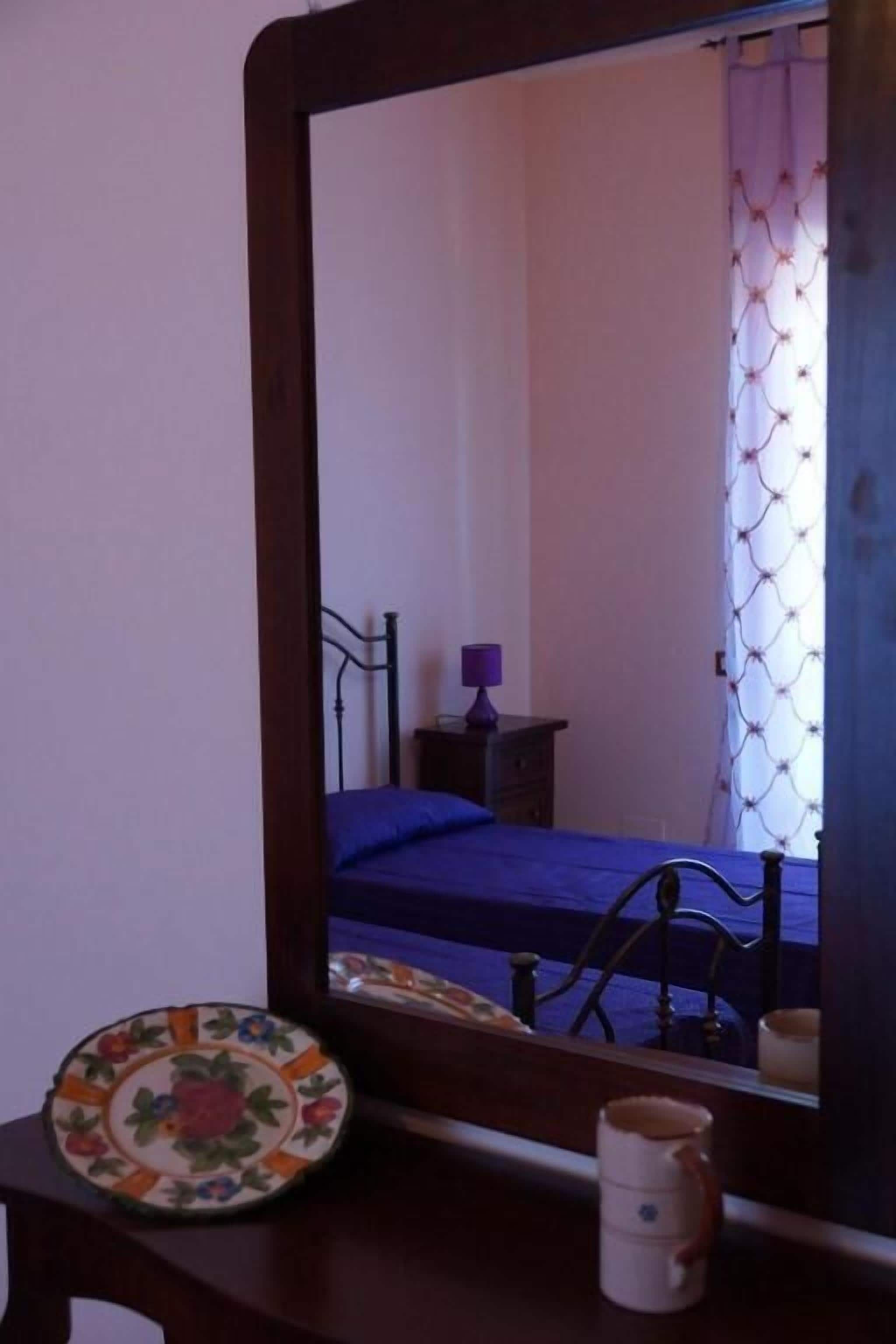Quarto com cama, mesa de cabeceira, espelho e janela com cortinas.