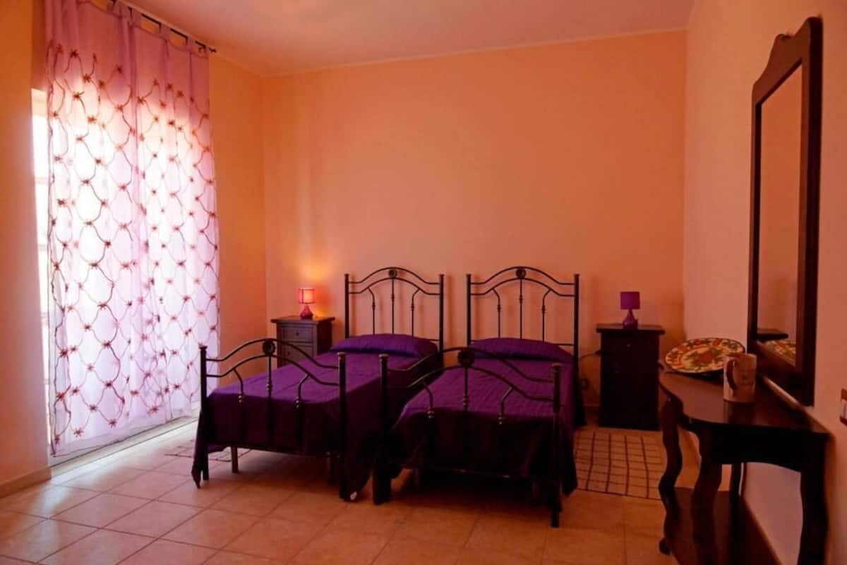 A bedroom with two beds, a bedside table with a lamp, a dresser, and a mirror.
