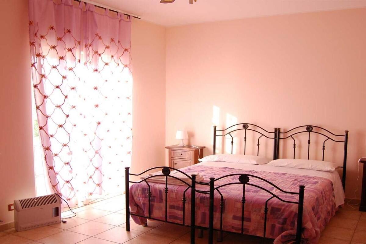 A bedroom with a bed, bedside tables, a radiator, and a window with curtains.