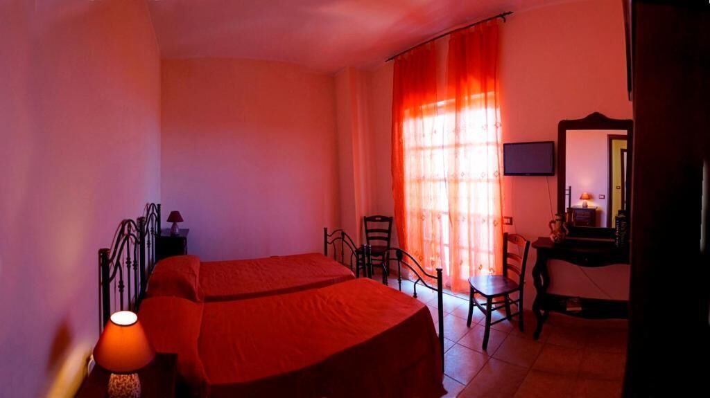 A bedroom with a bed, a desk, a chair, a lamp, and a mirror.