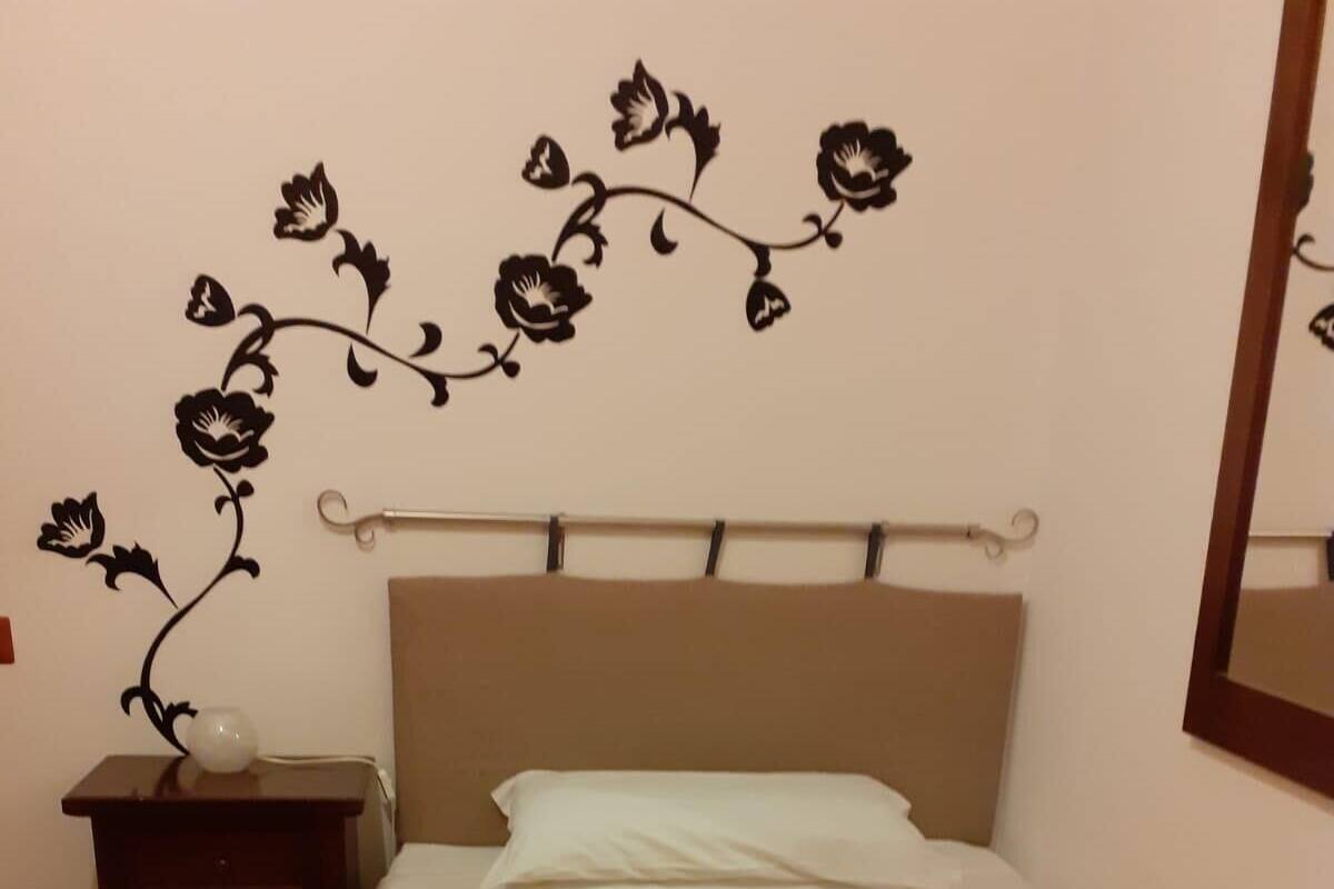 A bedroom with a bed, a nightstand, a wall-mounted shelf, and a mirror.