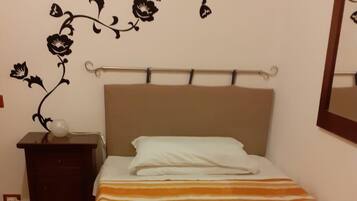 Un dormitorio con cama, mesita de noche, estante en la pared y espejo.