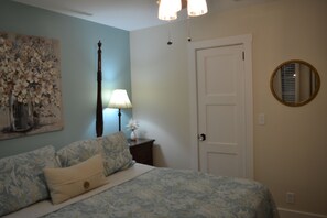 A bedroom with a bed, a nightstand, a lamp, a door, and a wall-mounted mirror.
