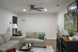 A living room with a ceiling fan, a sofa, a coffee table, and a TV on a stand.