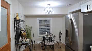 Cuina amb nevera d'acer inoxidable, taula de dinar amb quatre cadires, un lampadari i una finestra amb persianes.