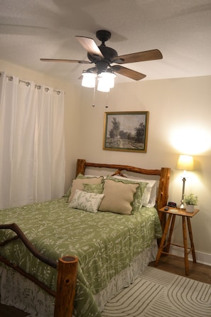 A bedroom with a bed, a ceiling fan, a nightstand, a lamp, and a framed picture on the wall.