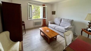 A room with a grey sofa, a wooden coffee table, a white armchair, a wooden cabinet, and a window with curtains. - 3-room apartment in a residential complex. (11100 narbonne)