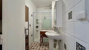 A bathroom with white tiles, a sink, a mirror, and a shower area. - 3-room apartment in a residential complex. (11100 narbonne)