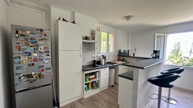 A modern kitchen with a refrigerator covered in magnets, a microwave, and a coffee maker. - 3-room apartment in a residential complex. (11100 narbonne)
