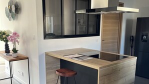 Moderni keittiö, jossa on keskeinen keittiösaareke, baarituolit, sisäänrakennettu uuni ja suuri ikkuna.