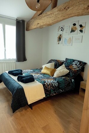 Une chambre à coucher avec un lit, une poutre en bois au plafond, une fenêtre avec des rideaux et des œuvres d’art murales.