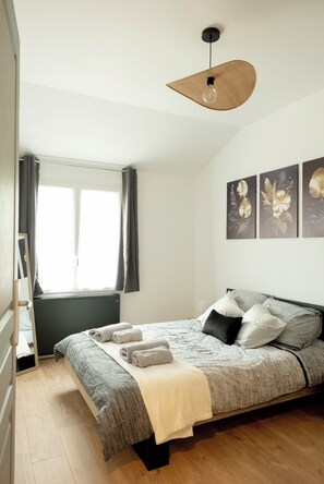 A bedroom with a bed, a hanging light fixture, a radiator, and a window with curtains. - Elegant house 100m2, garden, relaxation and comfort (Portets)