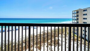 Vista de la playa desde un balcón, con cielo despejado, arena y un edificio de varios pisos con balcones.