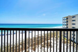 Blick auf den Strand vom Balkon aus, mit blauem Himmel, Sandstrand und einem mehrstöckigen Gebäude mit Balkonen.
