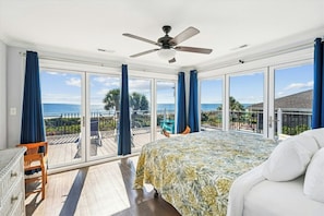 Ein Schlafzimmer mit einem großen Bett, einem Deckenventilator und Blick auf das Meer durch große Fenster.