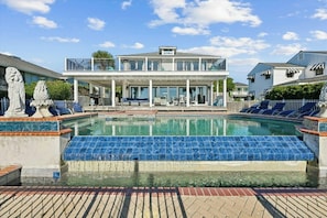 Ein Pool mit blauen Fliesen, eine überdachte Terrasse und ein zweistöckiges Gebäude mit einem Balkon.