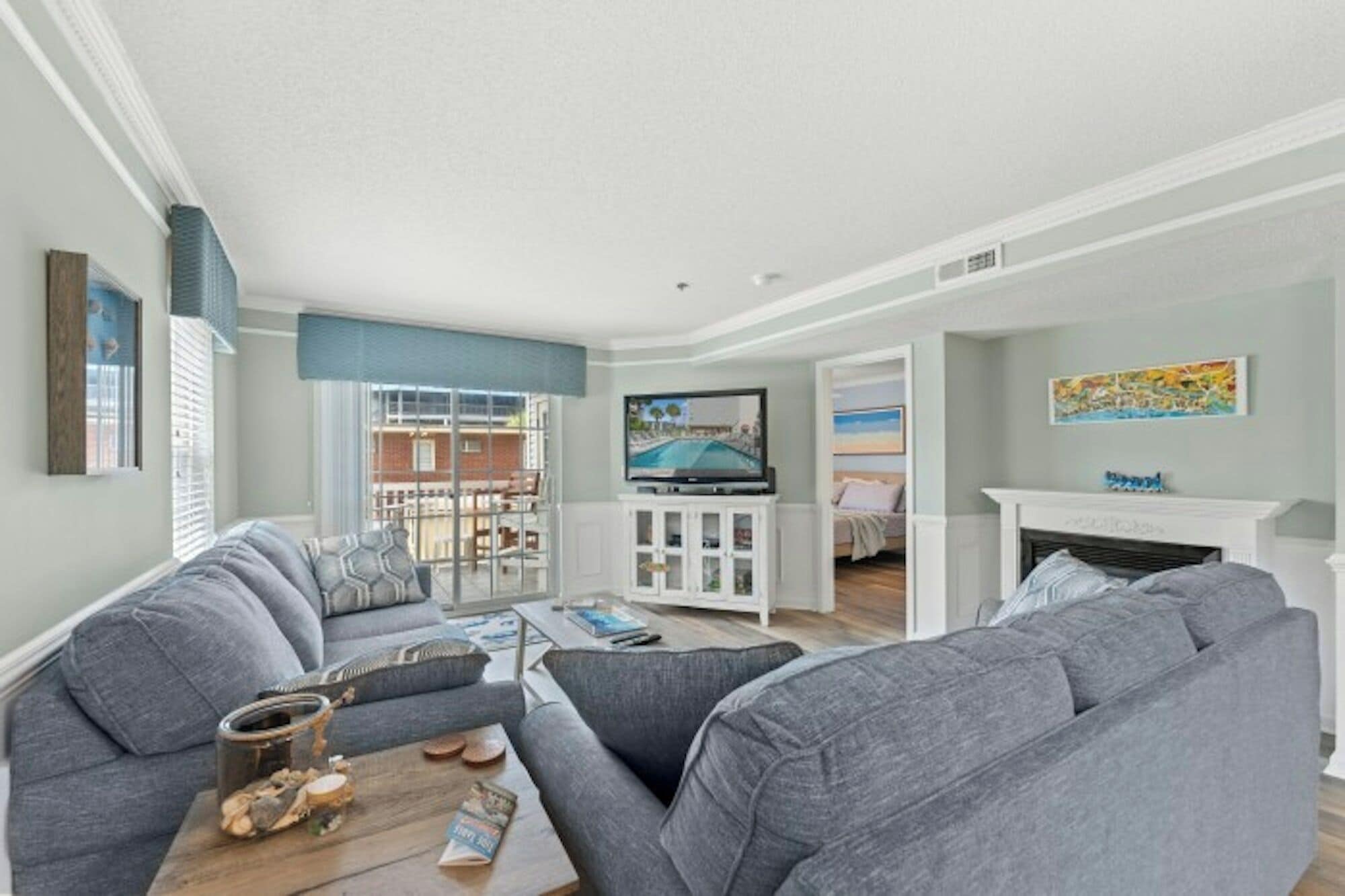 A living room with a grey sofa, a coffee table with books, a television, and a fireplace.