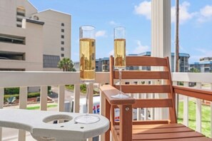 Ein Balkon mit zwei Sektgläsern, einem Holzstuhl und einem weißen Tisch.