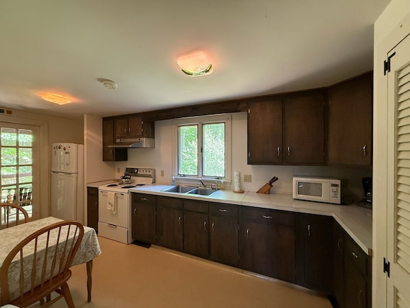 Una cocina compacta con armarios de madera, estufa, lavamanos y ventana.