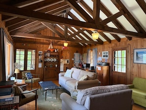 Interior acogedor de una cabaña con techo de madera, un sofá, una mesa de comedor y una zona de cocina.