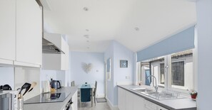 Een moderne keuken met witte kastjes, een roestvrijstalen afzuigkap, een raam met uitzicht en een spoelbak met afwasservice.