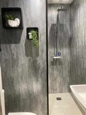 Un baño moderno con pared de concreto, ducha con cabezal de mano y bañera blanca.