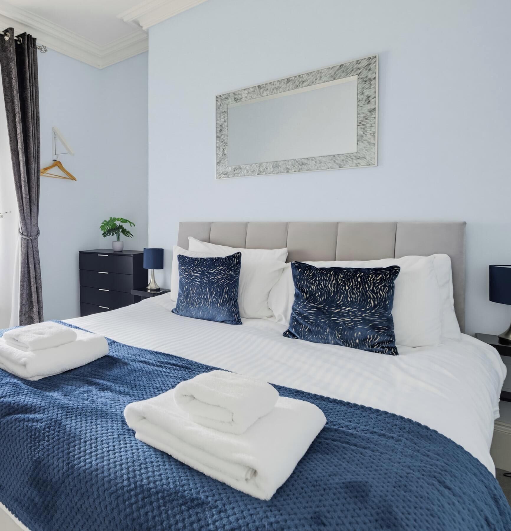A hotel room with a bed, a bedside table, a lamp, a hanging plant, and a mirror on the wall.