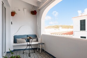 Un balcon avec un mur blanc, un canapé bleu, une petite table ronde et une plante suspendue.