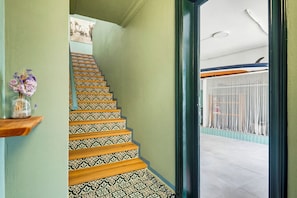 Eine Treppe mit gemusterten Fliesen, einem Holzgeländer und Blick auf einen Balkon mit Geländer.