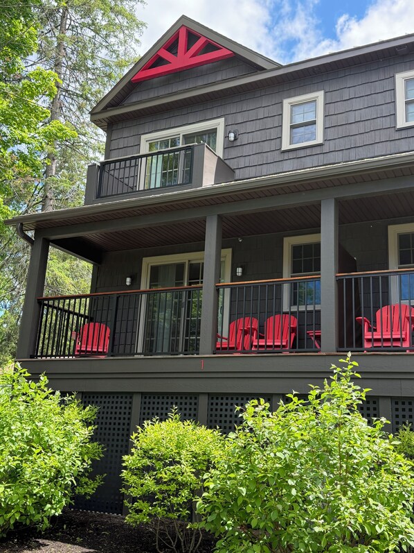Una casa de dos pisos con un balcón, sillas rojas y un diseño de techo rojo.