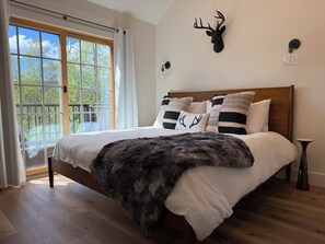 Un dormitorio con una cama grande, una cabeza de venado montada, una lámpara de vidrio y vistas a través de una ventana.
