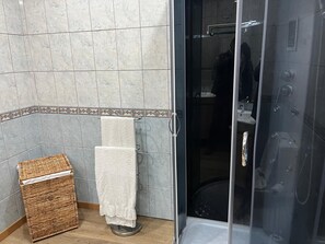 Ein Badezimmer mit Duschkabine aus Glas, einem Korbwäscheschrank und einem Handtuchhalter.